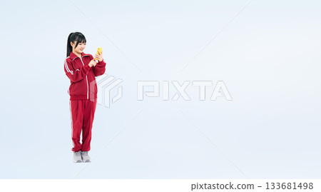 Full-body photo of a female student wearing a gym jersey using a smartphone 133681498