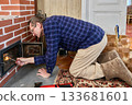 Lighting fire in wood brick stove, middle aged man uses gas lighter, kneeling in front of stove opening. 133681601