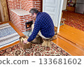 Mature man lights wood stove in country house. 133681602