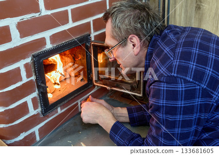 Wood stove heating country house middle aged man maintains fire brick wood burning stove. 133681605