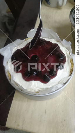 Blueberry sauce spooned over whipped cream cheesecake with graham crust, enticing dessert presentation and glossy berry topping Blueberry sauce spooned over whipped cream cheesecake with graham crust, enticing dessert presentation and glossy berry topping 133681802