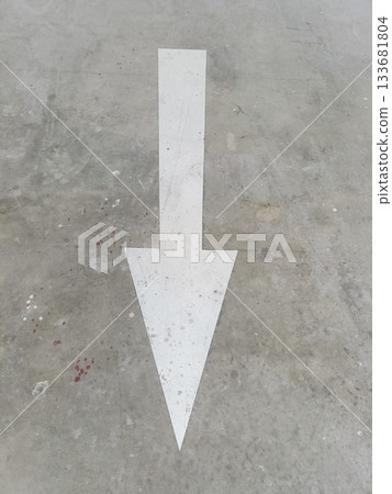 White directional arrow painted on concrete floor pointing forward, minimal urban graphic with worn texture 133681804