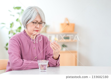 A silver-haired senior woman checking the dosage and capacity of a medicine bottle 133682180