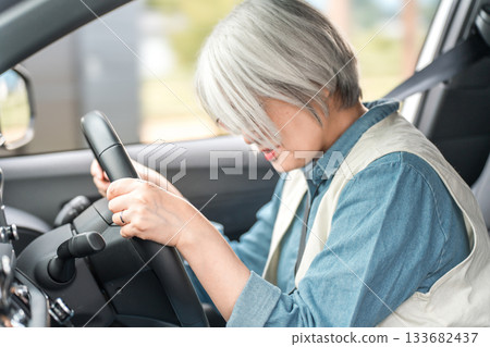 An elderly driver woman who falls asleep while driving a car 133682437