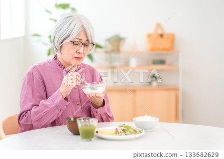 A gray-haired senior woman eating in the dining room at home A gray-haired senior woman eating in the dining room at home 133682629