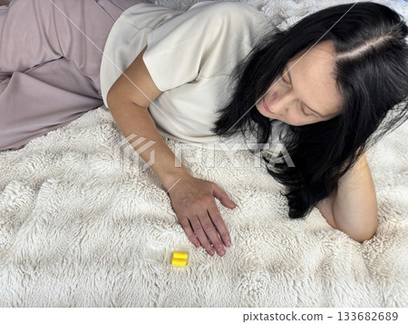 Woman lying on a bed while examining yellow foam earplugs used for noise reduction, sleep quality improvement, and nighttime comfort Woman lying on a bed while examining yellow foam earplugs used for noise reduction, sleep quality improvement, and nighttime comfort 133682689
