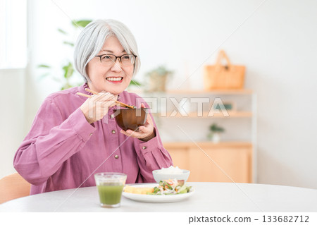 A gray-haired senior woman eating in the dining room at home 133682712