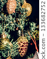 The green Christmas tree is decorated with gold baubles and glittering ornaments, creating vibrant reflections and a winter holiday atmosphere. 133682752