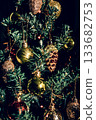 The green Christmas tree is decorated with gold baubles and glittering ornaments, creating vibrant reflections and a winter holiday atmosphere. 133682753