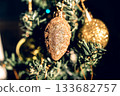 The green Christmas tree is decorated with gold baubles and glittering ornaments, creating vibrant reflections and a winter holiday atmosphere. 133682757