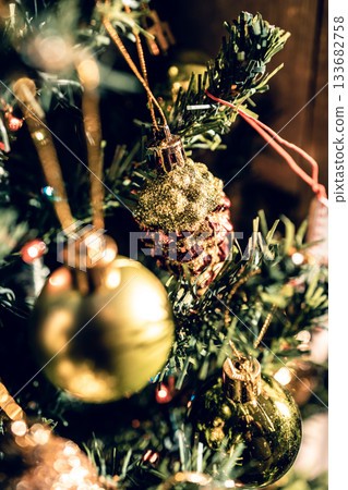 The green Christmas tree is decorated with gold baubles and glittering ornaments, creating vibrant reflections and a winter holiday atmosphere. The green Christmas tree is decorated with gold baubles and glittering ornaments, creating vibrant reflections and a winter holiday atmosphere. 133682758