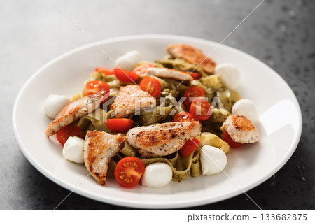 fettuccine with pesto, tomatoes , mozzarella and chicken on white plate 133682875