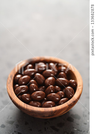 Milk chocolate dragee in olive wood bowl on concrete background Milk chocolate dragee in olive wood bowl on concrete background 133682878