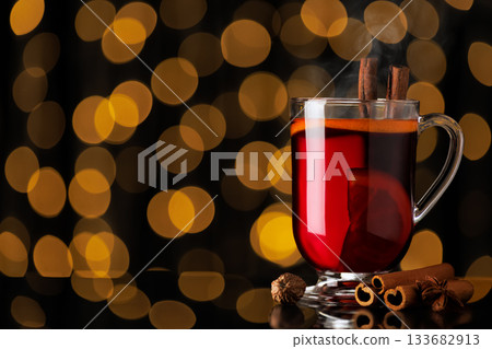 steaming hot mulled wine with cinnamon and anise stars in glass mug on black background with bokeh lights steaming hot mulled wine with cinnamon and anise stars in glass mug on black background with bokeh lights 133682913