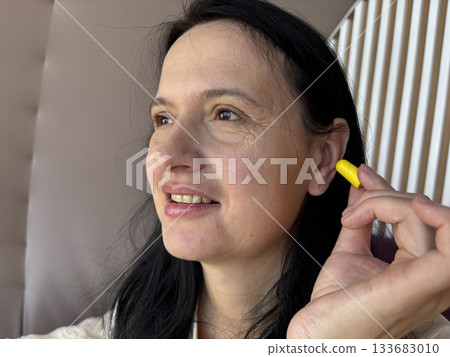 Calm brunette woman using yellow foam earplugs for better sleep and noise protection at home, peaceful bedtime routine for quiet rest and relaxation 133683010