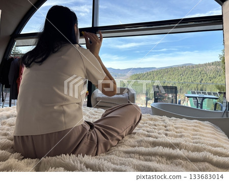 Relaxed woman with earplugs sitting by a window enjoying quiet moments and peaceful silence during travel or rest at home 133683014