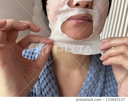 Mature woman applying a moisturizing sheet facial mask at home. Anti aging skincare routine for mature skin, hydration, rejuvenation, fine lines treatment, beauty self care concept Mature woman applying a moisturizing sheet facial mask at home. Anti aging skincare routine for mature skin, hydration, rejuvenation, fine lines treatment, beauty self care concept 133683137