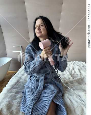 Woman Drying Hair With Compact Pink Hair Dryer at Home, Daily Beauty Routine in Cozy Bathrobe Woman Drying Hair With Compact Pink Hair Dryer at Home, Daily Beauty Routine in Cozy Bathrobe 133683274