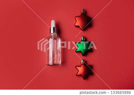 Cosmetic serum on red background with red and green star shaped Christmas ornaments Cosmetic serum on red background with red and green star shaped Christmas ornaments 133683898