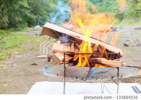 Fire and smoke from firewood burning in a campfire 133684316