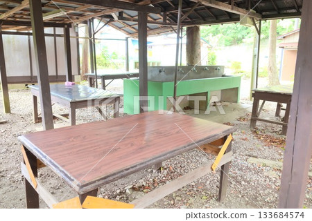 Campsite outdoor kitchen space with cooking hut and work tables 133684574