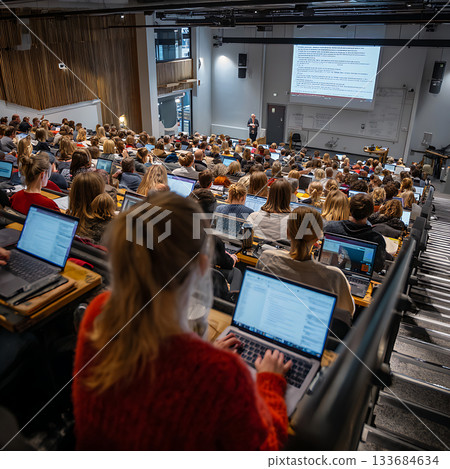 A large, modern lecture hall filled with students using laptops 133684634
