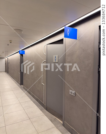 Grey interior of shopping center corridor with public restrooms for men and women, with blue signs on wall. WC entrance features gender symbols. Door to restrooms is separate for men and women Grey interior of shopping center corridor with public restrooms for men and women, with blue signs on wall. WC entrance features gender symbols. Door to restrooms is separate for men and women 133684712