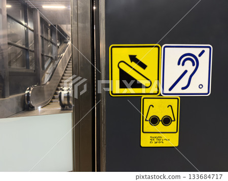 Set of signs for people with disabilities with direction to escalator. Signs for deaf and blind people with braille text at entrance to escalator with accessible area for handicapped people 133684717