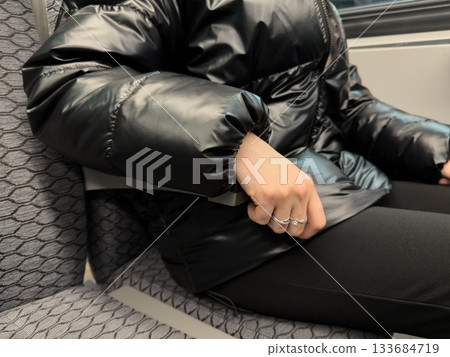 Girl hand on armrest of train with seats. Close up photo of armrest being used on public transport. Woman in warm clothing using retractable armrest. Hand in black jacket holds onto armrest of seat 133684719