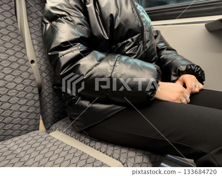 Close up photo of girl body sitting in train seat during trip on seated commuter train. Train ride is in cold weather. Woman is wearing clothing while sitting in train seat Close up photo of girl body sitting in train seat during trip on seated commuter train. Train ride is in cold weather. Woman is wearing clothing while sitting in train seat 133684720