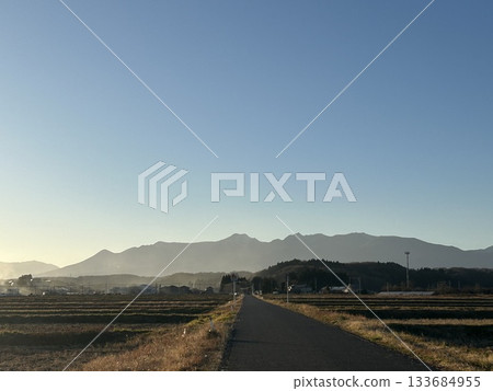 A single road stretching through a quiet rural village and a mountain range in the evening light A single road stretching through a quiet rural village and a mountain range in the evening light 133684955