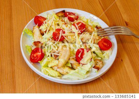 Fresh healthy caesar salad with chicken breast, cherry tomatoes, lettuce, parmesan cheese, dressing and croutons on wooden table Fresh healthy caesar salad with chicken breast, cherry tomatoes, lettuce, parmesan cheese, dressing and croutons on wooden table 133685141