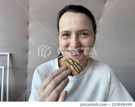 Smiling adult woman eating, tasting cookies while resting on the bed, cozy breakfast or snack moment in a bright peaceful bedroom Smiling adult woman eating, tasting cookies while resting on the bed, cozy breakfast or snack moment in a bright peaceful bedroom 133686484