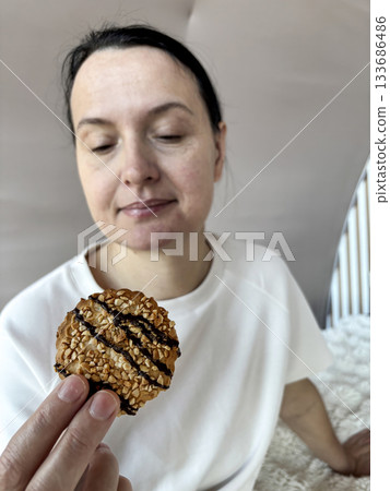 Smiling adult woman eating, tasting cookies while resting on the bed, cozy breakfast or snack moment in a bright peaceful bedroom Smiling adult woman eating, tasting cookies while resting on the bed, cozy breakfast or snack moment in a bright peaceful bedroom 133686486