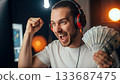 Excited gamer celebrates victory with cash in hand and a winning expression 133687475