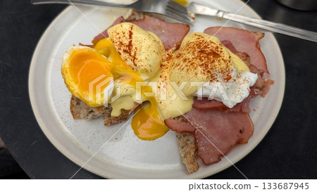 A plate of Eggs Benedict with runny yolk on the toast and bacon A plate of Eggs Benedict with runny yolk on the toast and bacon 133687945