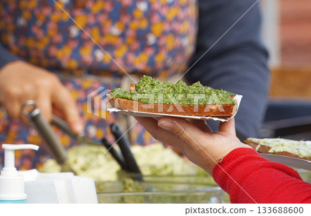 Customer holding basil pesto toast at Prague farmers market 133688600