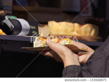 Person holding a slice of savory pie at a street food festival Person holding a slice of savory pie at a street food festival 133688675