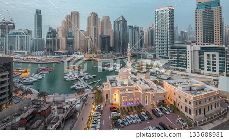 Yachts in Dubai Marina flanked by the Al Rahim Mosque and residential towers and skyscrapers aerial day to night timelapse. 133688981
