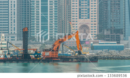 Excavator and modern skyscrapers in Dubai city at morning timelapse from the Palm Jumeirah Island. 133689536