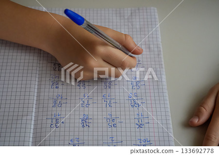 Close-up of a hand holding a pen and writing in a notebook with examples. Face not visible. Focus on studying, homework, and learning. Close-up of a hand holding a pen and writing in a notebook with examples. Face not visible. Focus on studying, homework, and learning. 133692778