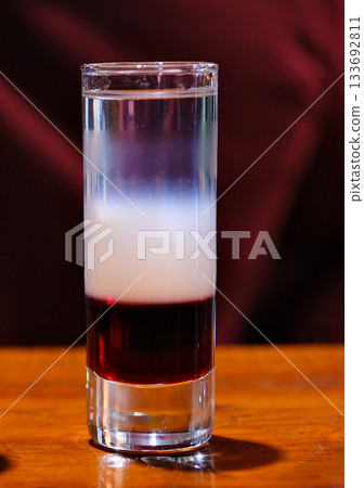 Layered cocktail shot flaming layered cocktail shot in a glass with blue fire on top, isolated on black background with reflection. 133692811