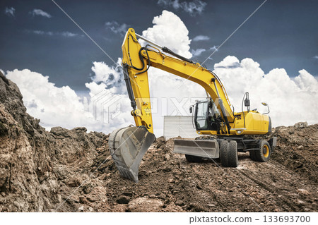 A powerful yellow excavator digs into the ground at a construction site during the day, showcasing its large bucket and articulated arm A powerful yellow excavator digs into the ground at a construction site during the day, showcasing its large bucket and articulated arm 133693700