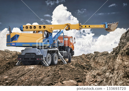 Construction workers operate a large crane and truck on a site with dirt piles and clouds in the background, indicating active work and progress Construction workers operate a large crane and truck on a site with dirt piles and clouds in the background, indicating active work and progress 133693720