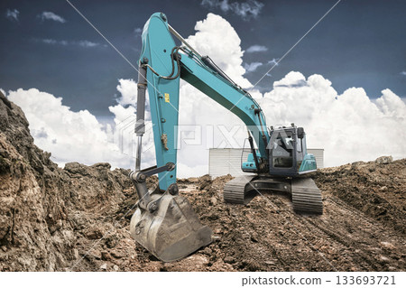 Heavy machinery digs into the earth at a construction site. The excavator's arm extends, preparing for the next move in the afternoon light Heavy machinery digs into the earth at a construction site. The excavator's arm extends, preparing for the next move in the afternoon light 133693721