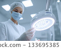 A female doctor in a mask and gloves adjusts a surgical lamp before surgery 133695385