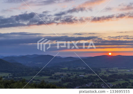 Sun setting behind rolling mountains in green valley Sun setting behind rolling mountains in green valley 133695555