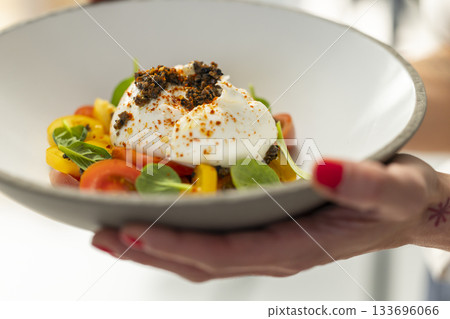 Hand serving fresh burrata salad with colorful tomatoes 133696066
