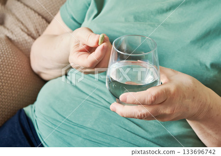 Senior woman with overweight taking daily supplement with glass of water Senior woman with overweight taking daily supplement with glass of water 133696742