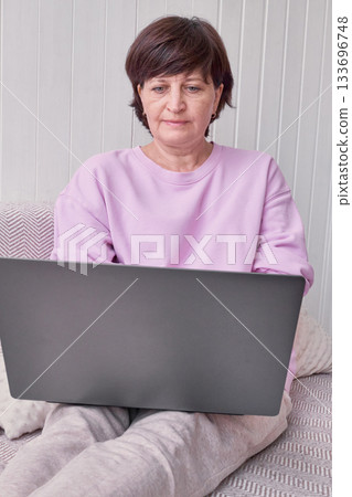 Caucasian mature female using laptop at home in pink sweater. 133696748